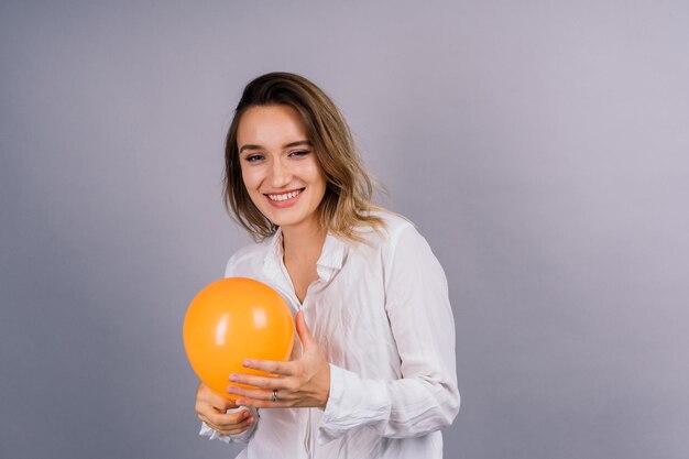 Close-up-Porträt einer jungen Frau, die einen Ballon auf einem isolierten grauen Hintergrund aufbläst