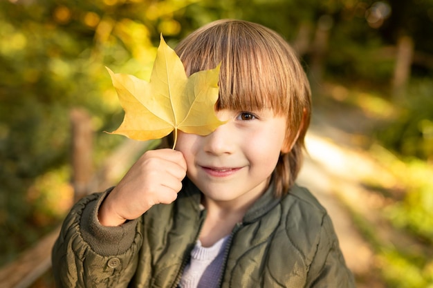 Foto close-up-porträt eines jungen mit einem ahornblatt in der hand im herbst kleinkind junge geht in einem park in