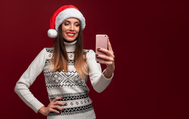 Close-up Porträt schöne weiße Frau in rotem Weihnachtsmann Hut auf rotem Studio-Hintergrund Weihnachten und