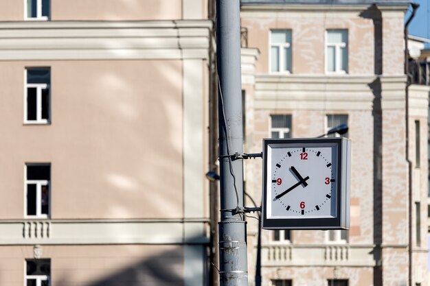 Close-up de un reloj de calle cuadrado colgado de un pilar con el telón de fondo de una pared de ladrillos de un edificio