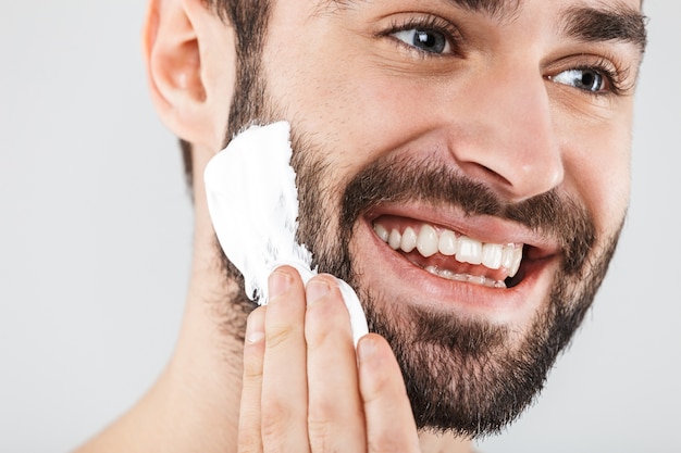 Close Up retrato de un apuesto hombre barbudo que se encuentran aisladas sobre blanco, aplicando espuma de afeitar