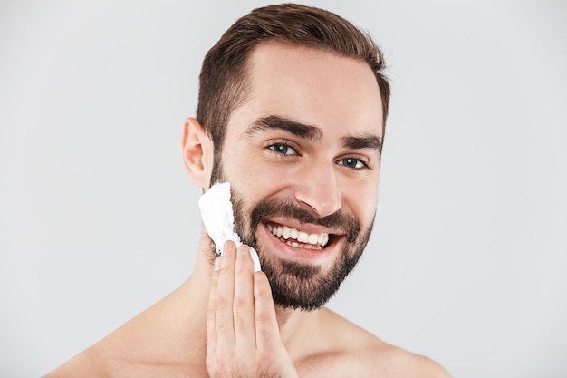 Close Up retrato de un apuesto hombre barbudo que se encuentran aisladas sobre blanco, aplicando espuma de afeitar