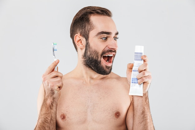 Close Up retrato de un apuesto hombre barbudo que se encuentran aisladas sobre blanco, mostrando pasta de dientes y cepillo de dientes