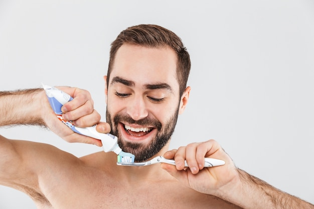 Foto close up retrato de un apuesto hombre barbudo que se encuentran aisladas sobre blanco, mostrando pasta de dientes y cepillo de dientes