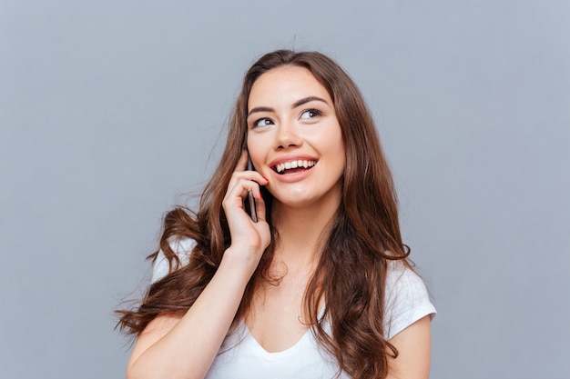 Close-up retrato de una bella mujer joven hablando por teléfono celular aislado en el fondo gris