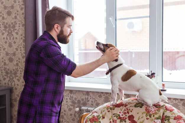 Close Up retrato bonito jovem hippie homem joga e ama seu bom amigo cachorro em casa. Emoções humanas positivas, expressão facial, sentimentos.