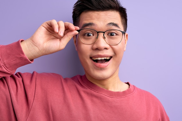 Close-up retrato de buen hombre chino en anteojos reacciona emocionalmente sobre algo, con la boca abierta