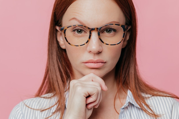 Close-up retrato de auto confiante empresário feminino detém o queixo, levanta a sobrancelha, usa óculos ópticos