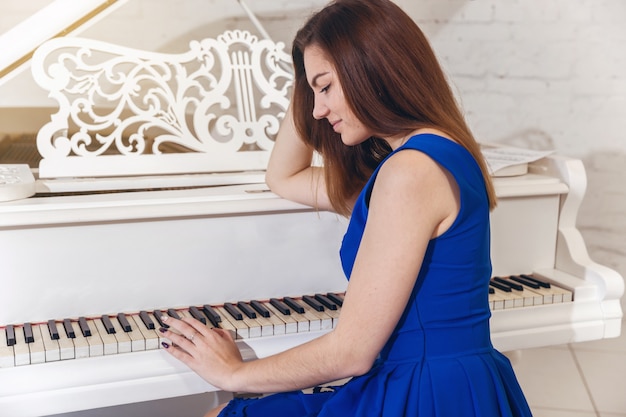 Close-up, retrato, de, um, menina, em, um, vestido azul, sentando, em, a, piano, e, toca, a, teclas piano