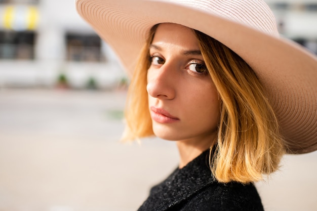 Close Up retrato de elegante elegante chica rubia de pelo corto con sombrero posando sobre la calle