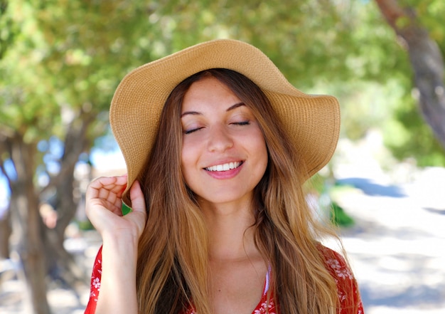 Close Up retrato de una hermosa niña sonriente con los ojos cerrados con un sombrero y un vestido rojo al aire libre