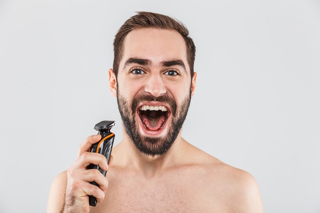 Close Up retrato de un hombre guapo con barba afeitado con una maquinilla de afeitar eléctrica aislado sobre blanco