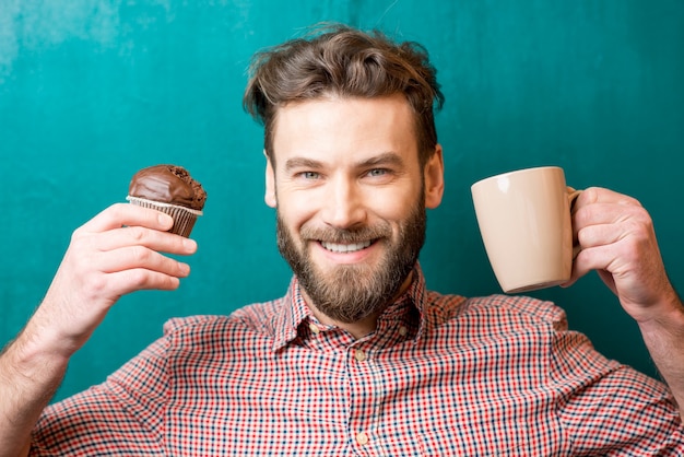 Close-up retrato de un hombre con muffin de chocolate y taza de café en el fondo verde