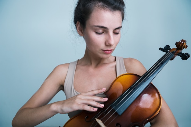 Close Up retrato de una joven y bella mujer posando con un violín aislado sobre fondo azul.