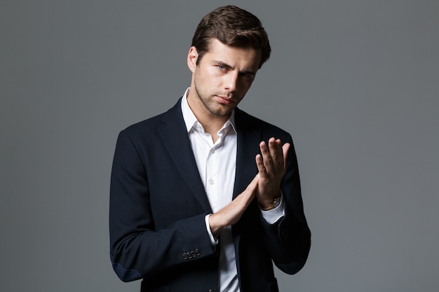 Close Up retrato de un joven empresario enfocado vestido con traje aislado sobre pared gris