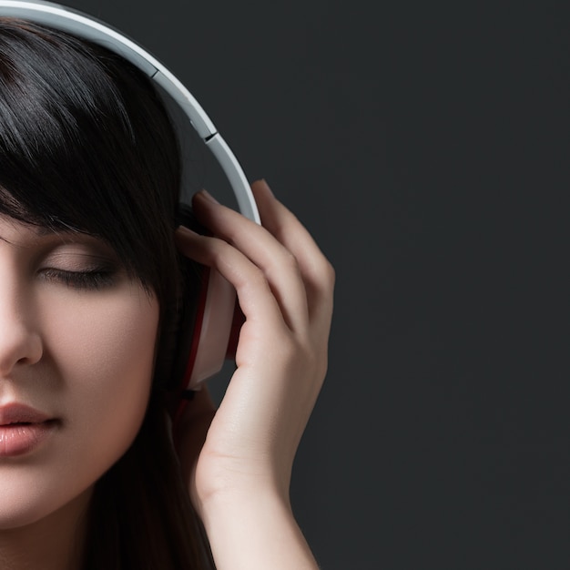 Close-up retrato de joven hermosa mujer morena escuchando música y sosteniendo auriculares blancos