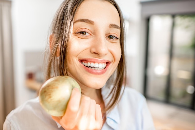 Close-up retrato de una joven mujer sonriente con manzana en la cocina