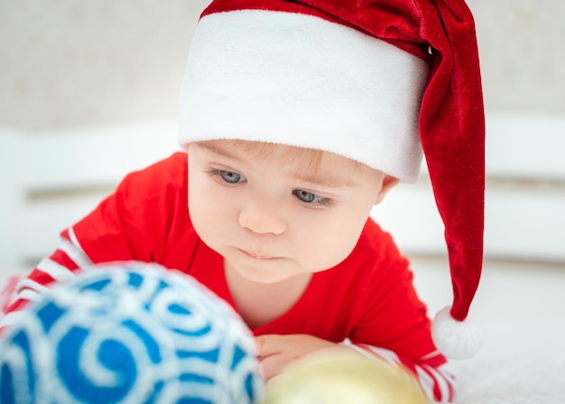 Foto close up retrato de lindo bebé caucásico vistiendo gorro de papá noel, bolas de navidad en primer plano nuevo