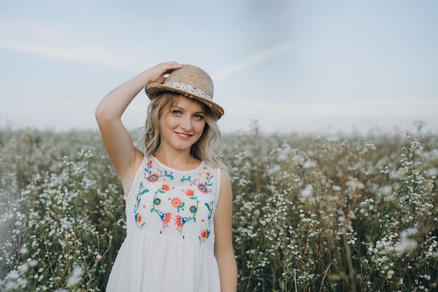 Close-up retrato menina com um chapéu na mão entra em um campo com flores do campo e sorri sinceramente