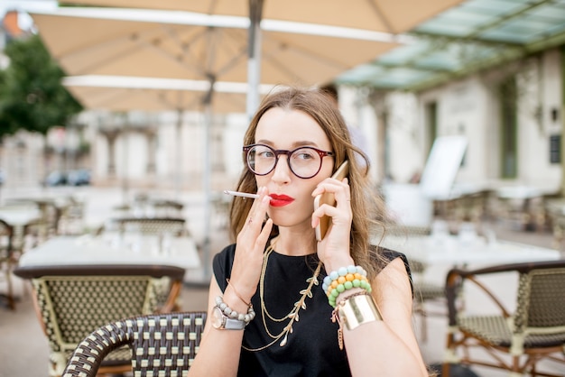 Close-up retrato de mujer fumadora hablando con el teléfono inteligente al aire libre en la terraza de un café típico francés en Francia