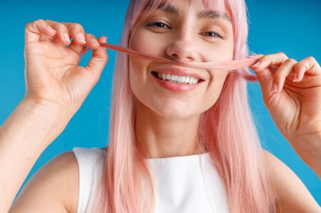 Close Up retrato de mujer joven feliz con largo cabello teñido de rosa natural sosteniendo un mechón de cabello como