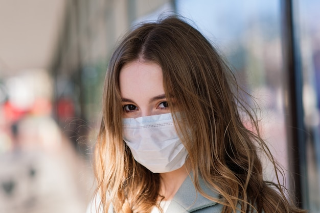 Close Up retrato de una mujer con una máscara médica y de pie en la calle frente a un café