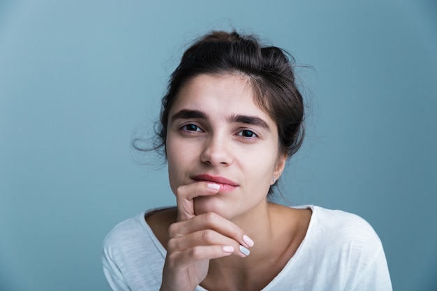 Close Up retrato de una mujer morena bastante joven con camiseta blanca que se encuentran aisladas sobre fondo azul, posando, tocando la cara