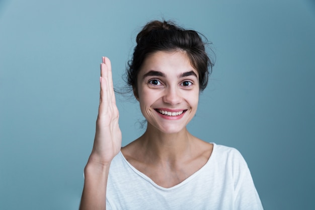 Close Up retrato de una mujer morena bastante joven con camiseta blanca que se encuentran aisladas sobre fondo azul, sosteniendo la mano hacia arriba