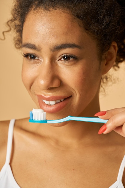 Close Up retrato de mujer de raza mixta joven natural cepillarse los dientes posando aislado sobre beige