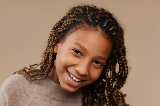 Close Up retrato de niña afroamericana despreocupada sonriendo felizmente a la cámara mientras está de pie contra el fondo beige en el estudio