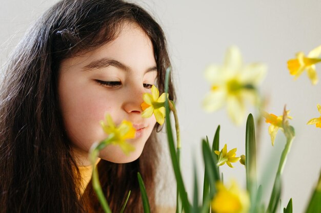 Foto close up retrato de niña de pelo oscuro viendo flores de narciso