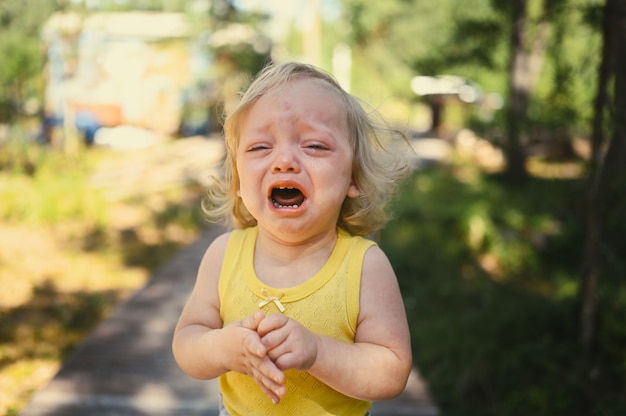 Close Up retrato de niño pequeño gracioso lindo niña rubia en traje amarillo llorando afuera