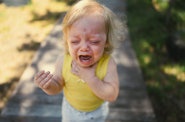 Close Up retrato de niño pequeño gracioso lindo niña rubia en traje amarillo llorando afuera