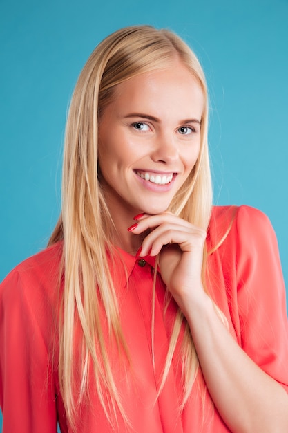 Close Up retrato de una sonriente chica rubia atractiva en vestido rojo mirando al frente aislado en una pared azul