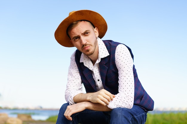 Close up retrato de viajero hombre casual con estilo guapo con sombrero sentado en la costa del mar y ...