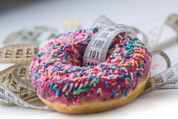 Close-up rosa gefrosteter Donut mit weißem Maßband.