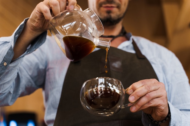 Close-up servindo café em uma xícara de vidro duplo em uma cafeteria pelo barista barbudo