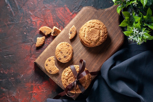 Close-up shot de deliciosos biscoitos de açúcar caseiros na placa de madeira e vaso de flores no fundo de cores misturas escuras
