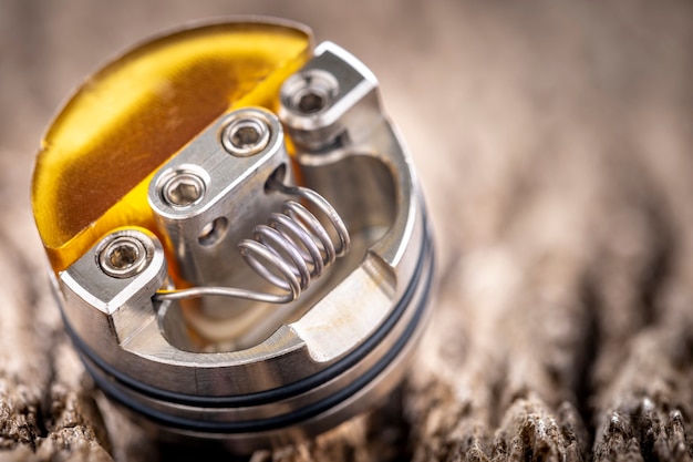 Close-up shot de space coil com ultem single coil redutor em atomizador de gotejamento reconstruível de ponta para caçador de sabores em fundo de textura de madeira natural rústica, dispositivo de vaporização