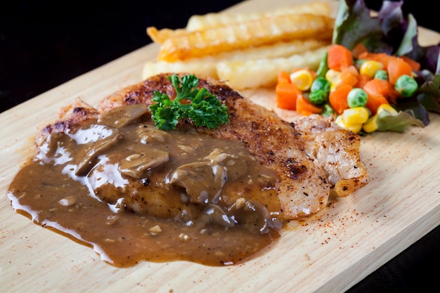 Close up Steak Schweinefleisch mit Pilzsauce, Pommes Frites und Salat auf Holzplatte.