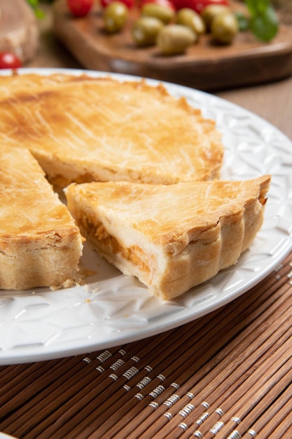 Close up Stück Chicken Pie mit Hüttenkäse, Tomaten, Zwiebeln und Oliven auf Holztisch und weißen Teller