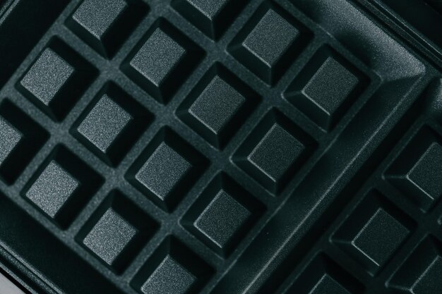 Close-up de una superficie de cuadrícula negra no pegajosa de los fabricantes de gofres Textura detallada del patrón de cuadrícula cuadrada utilizado para hornear gofres crujientes Diseño de electrodomésticos de cocina de alta calidad para cocinar en casa