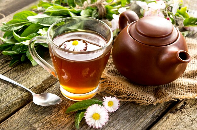 Close-up de té en una taza transparente con el telón de fondo de una tetera marrón sobre un fondo de madera