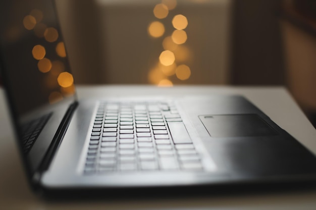 Close up del teclado del portátil con pantalla en blanco en una mesa por luces bokeh borrosas en el fondo