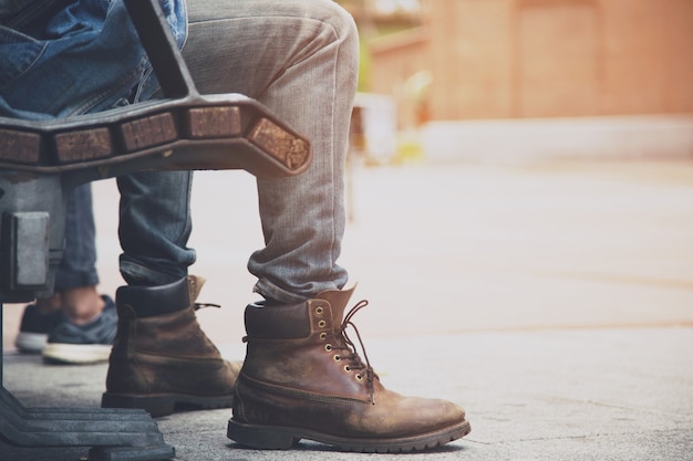 Close-up tênis tênis pessoas não identificadas hipster jovem sentar esperando em uma cadeira de madeira pública relaxante no parque público ao ar livre no centro da cidade.