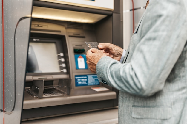 Foto close-up tiro da mão do homem sênior usando cartão de crédito do banco. ele digitando o código pin no teclado do caixa eletrônico.