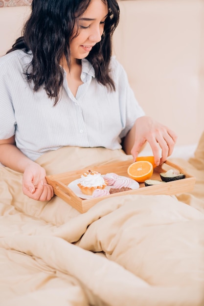 Close-up tiro de encantadora mulher morena bonita vestindo pijamas, sentado na cama, tomando café da manhã saboroso no quarto dela. conceito de guloso, estilo de vida, comida e refeição.