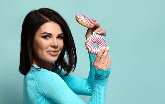 Foto close-up tiro de estúdio de uma bela mulher fitness com rosquinhas nas mãos mulher morena bonita seduz com rosquinhas doces em um fundo azul conceito de esportes e nutrição banner