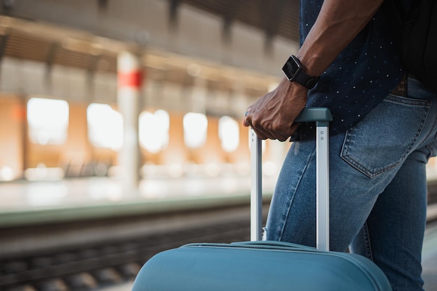 Close-up tiro de homem africano segurando uma mala em uma estação de trem enquanto ele está esperando o trem