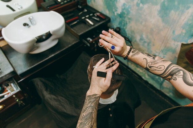 Foto close-up tiro de homem cortando o cabelo da moda na barbearia. o cabeleireiro masculino em tatuagens atendendo o cliente.